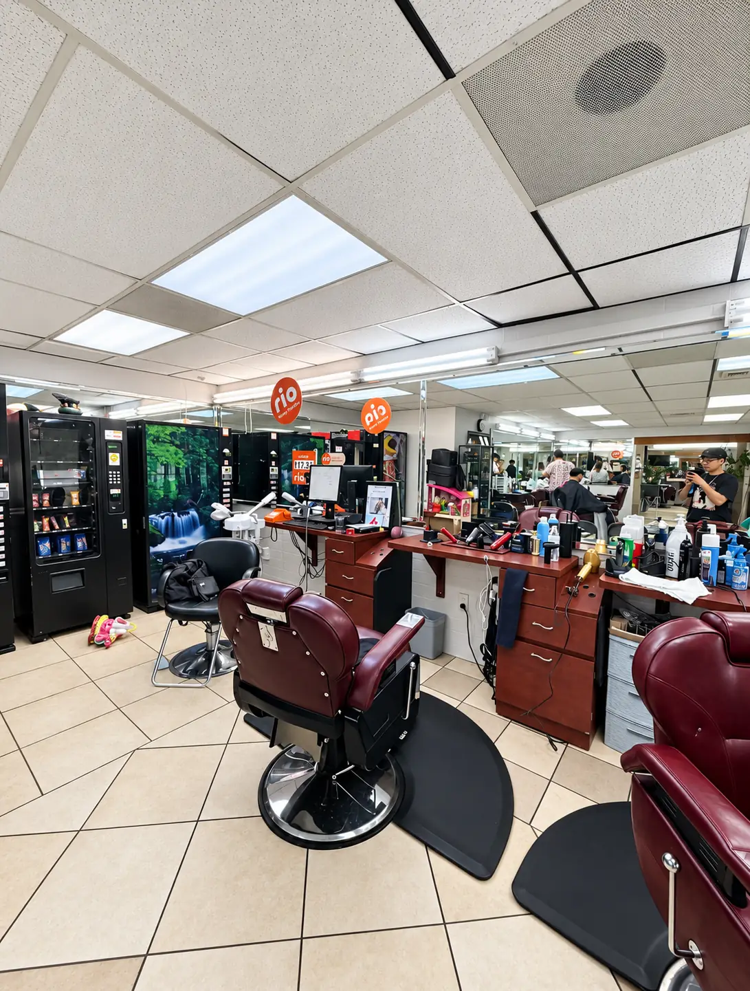 Several barber stations with burgundy chairs, wood cabinets and long mirrors along the wall of the shop